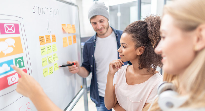 3 young people pointing at a content calendar on a white board.