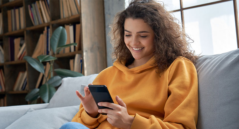 Woman wearing an orange sweatshirt looking at their phone.